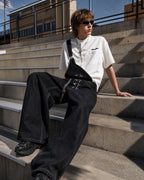 Black denim bib jeans with asymmetric shoulder strap, buckle details and wide legs
