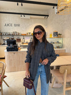 Woman wearing a grey checked plaid asymmetric blazer with long sleeves