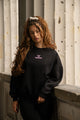 Women's black crewneck sweatshirt with pink chest logo